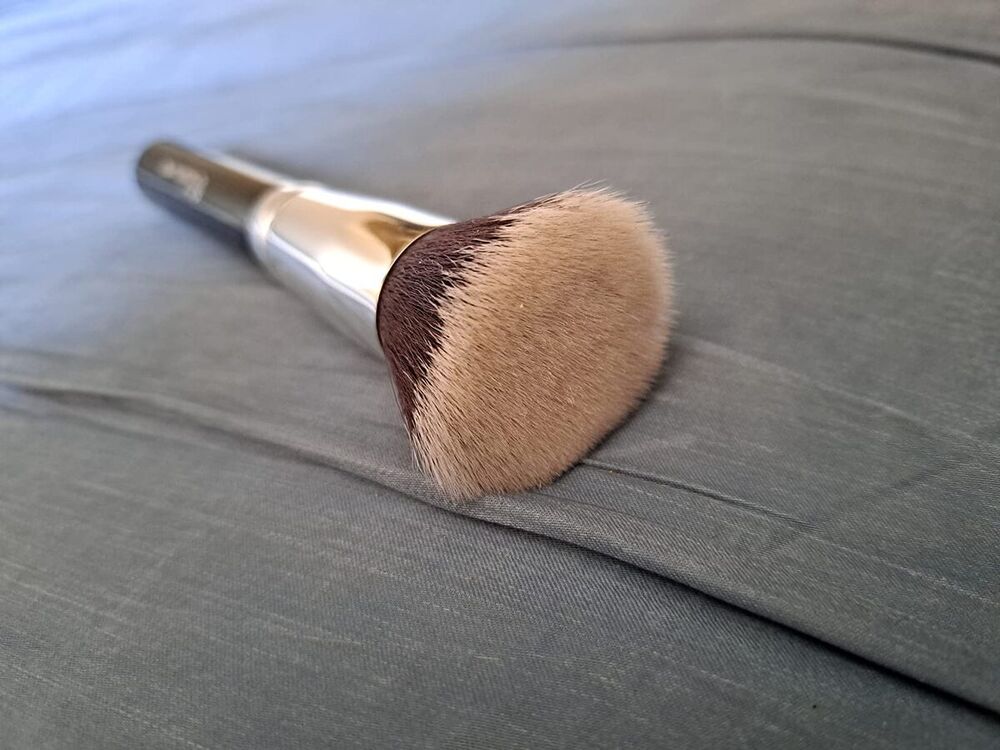 Pinceau kabuki à poils taupe posé sur un drap gris